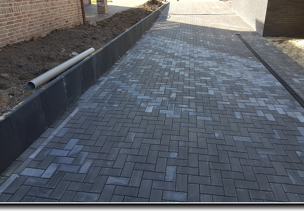 Oprit van zwarte betonklinkers met een keerwand naar een dieper gelegen garage